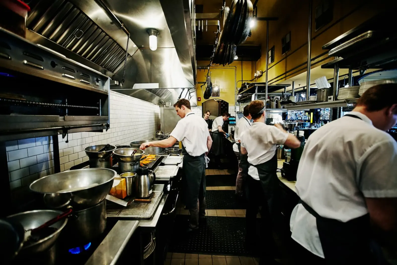 Chefs working under a commercial kitchen hood with gas burners